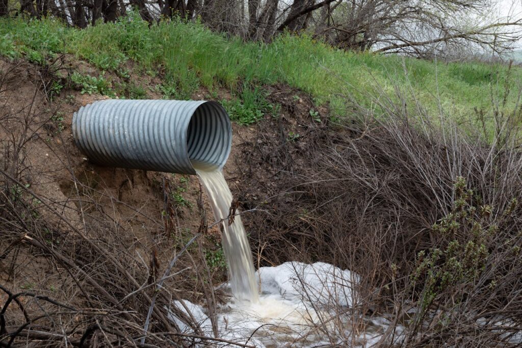 A rural drainage pipe pouring water into a natural ravine, surrounded by green vegetation.